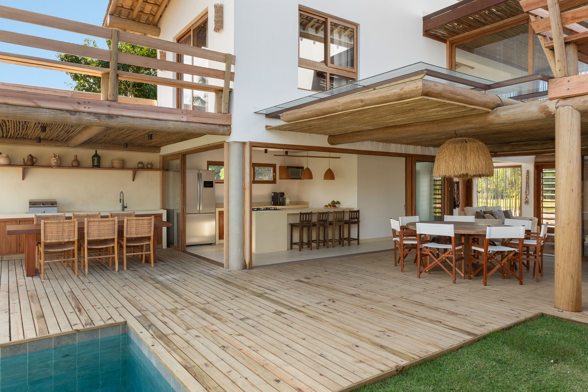 Wide deck beside the pool: the outdoor kitchen under the terrace, the kitchen opened to the deck, and the dining table under the pergola.