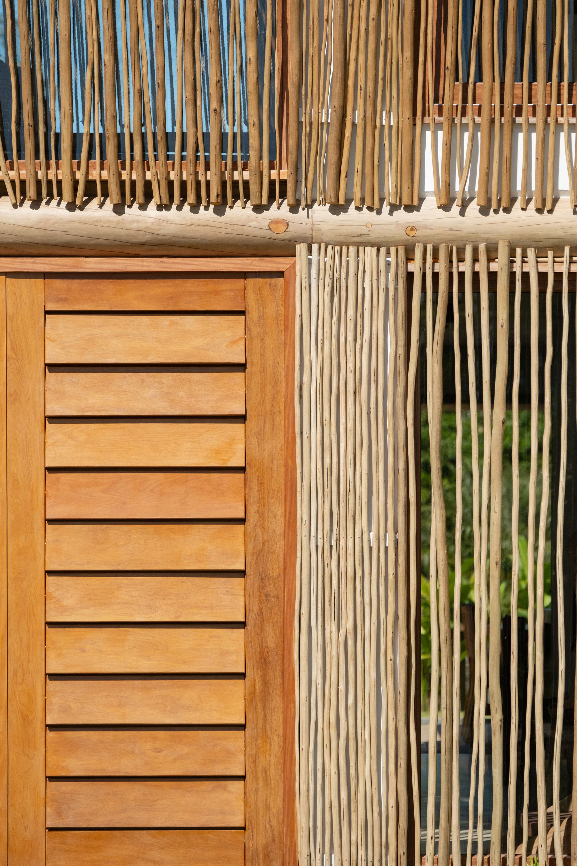Close-up where a louvred hardwood panel meets the stick screen, both hung from a round timber beam.