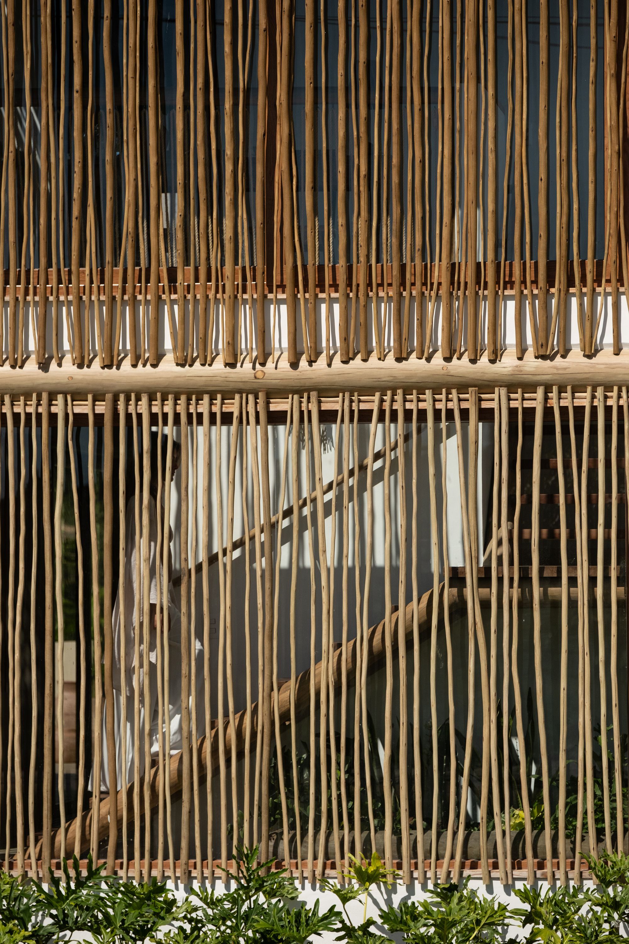A figure climbing the stair, seen faintly through the vertical timber sticks of the front screen.
