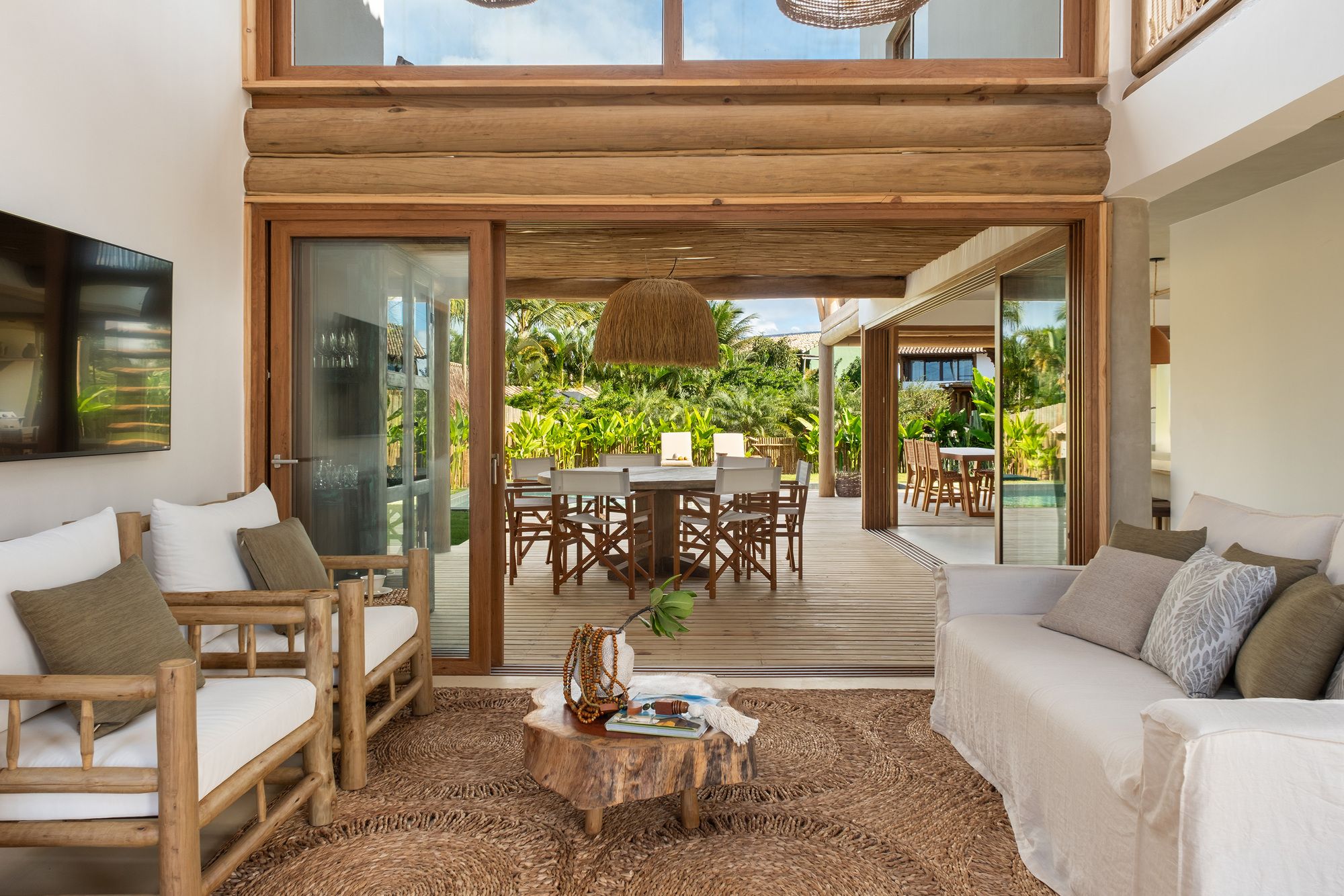 Living room looking through the open glazed wall to the dining table under the pergola and the garden beyond.
