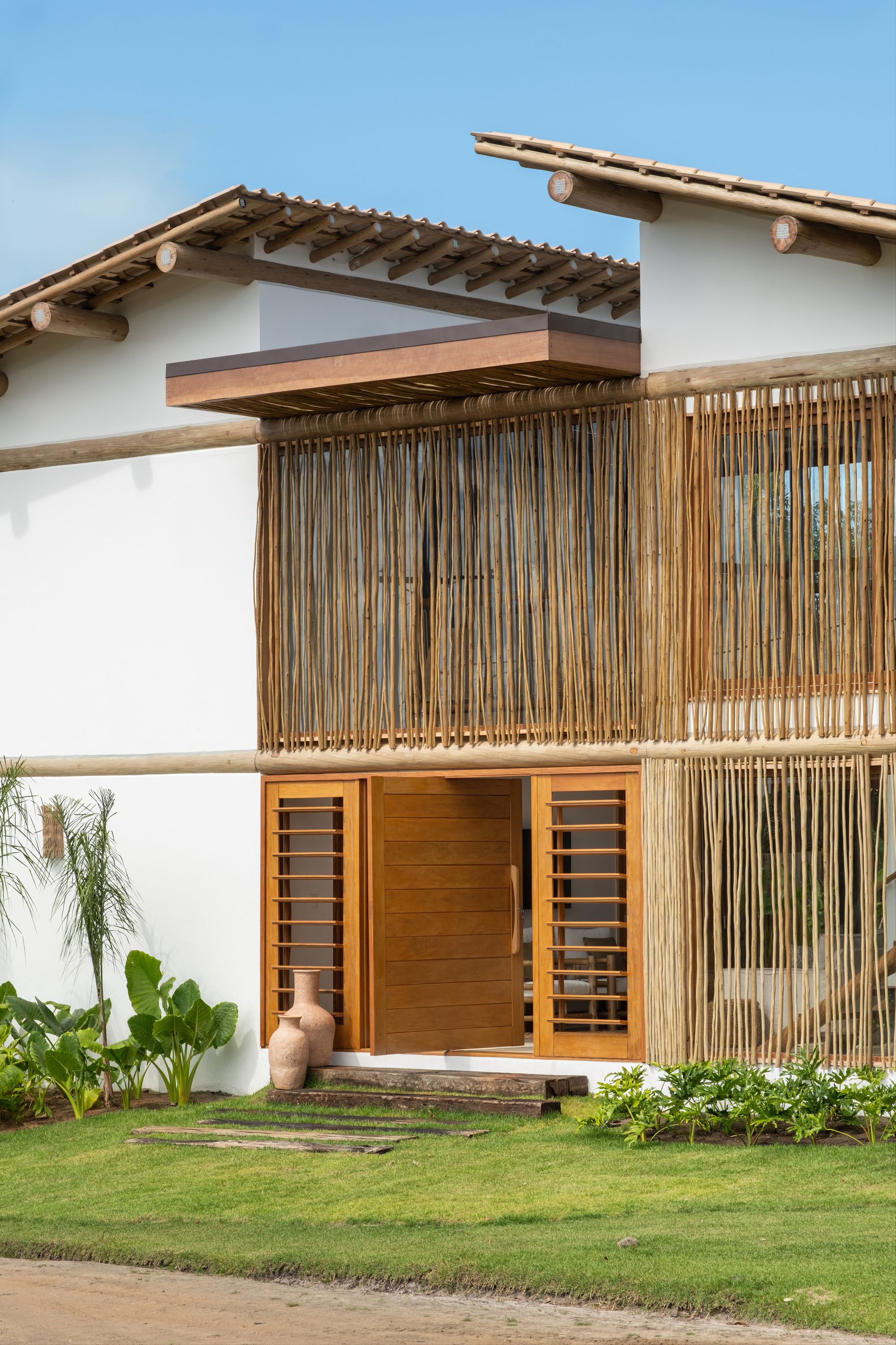 Angled view of the street front: the wooden pivot door stands open under a timber canopy, and the stick screen continues across the stair.