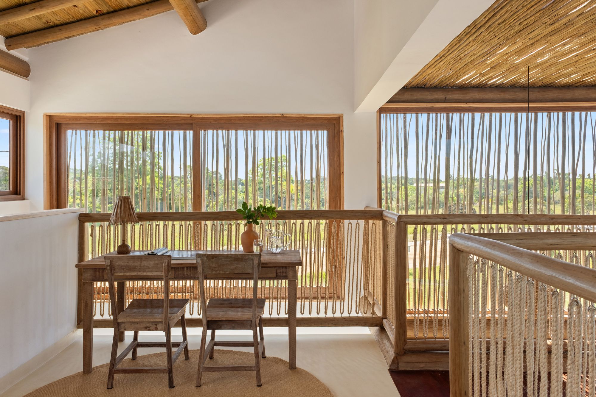 Upper landing with a timber desk and two chairs, looking through stick-screened windows over open grassland.