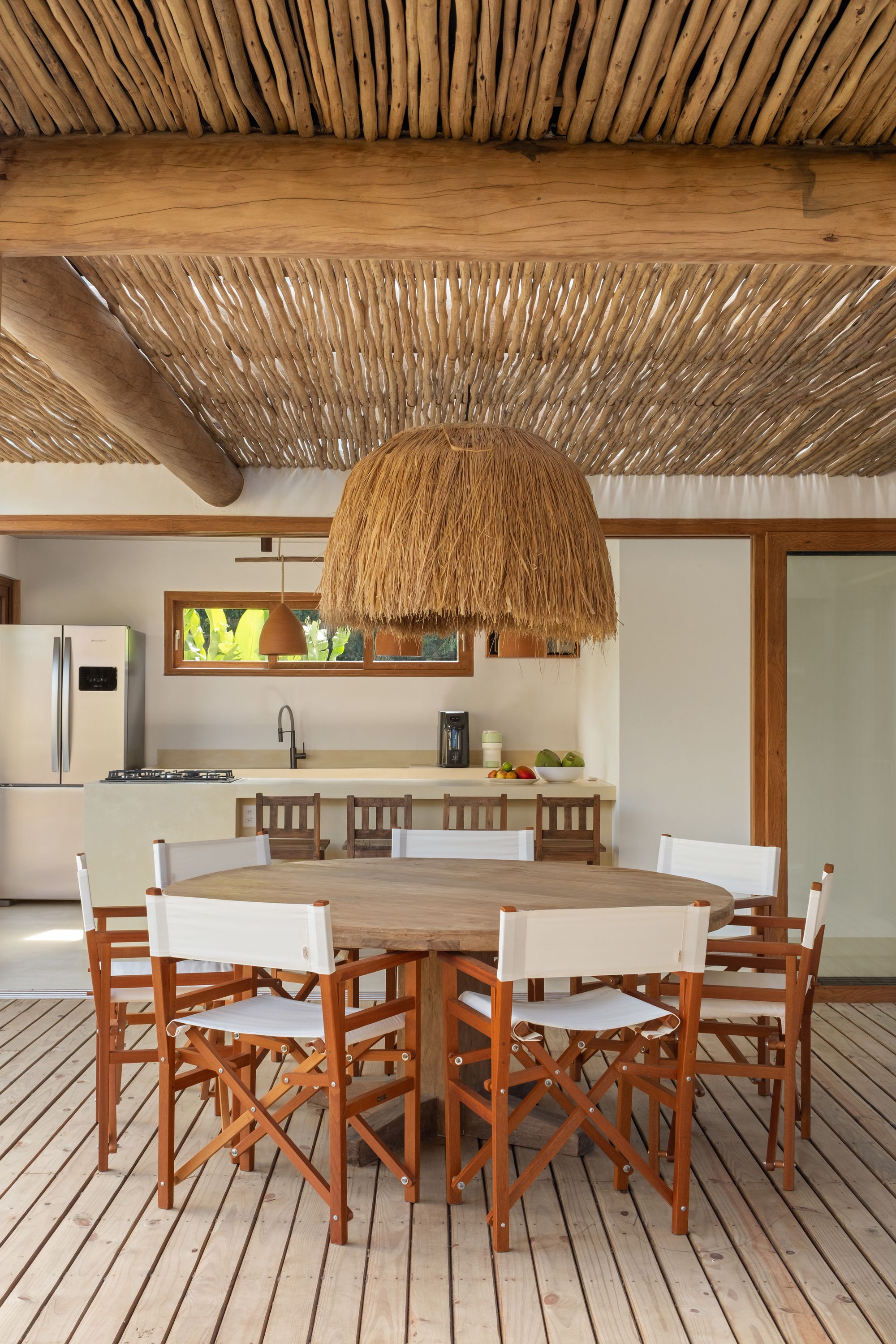 Dining table under the pergola, with the kitchen island and terracotta pendants behind.