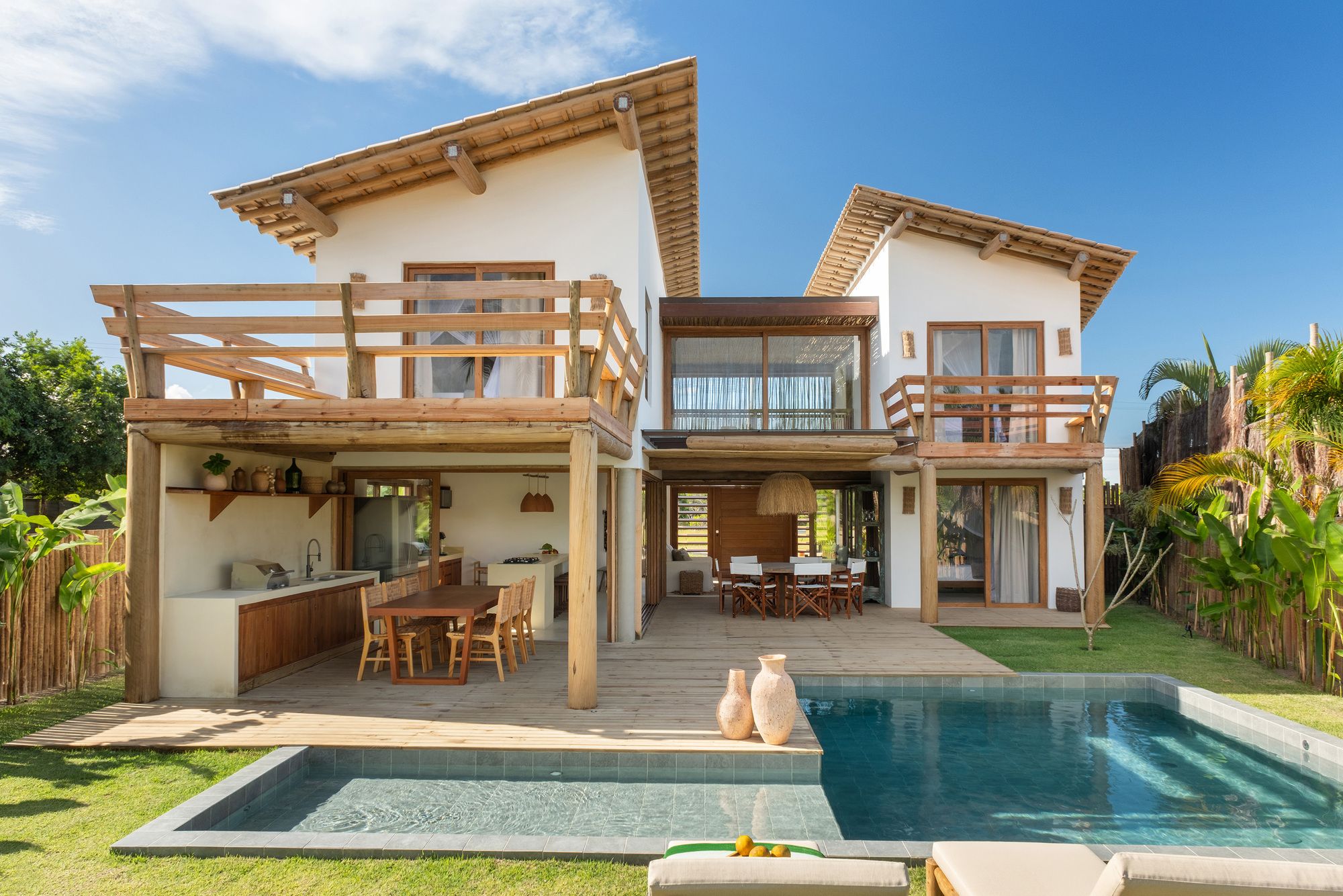 Garden side of the house opening onto the deck and an L-shaped pool, with a large timber terrace on the left and a small balcony on the right.